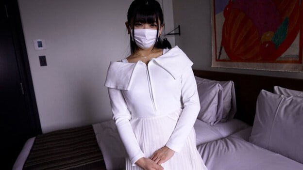 白い服とマスク姿の女性がベッドの前に立ち、両手を前で重ねる